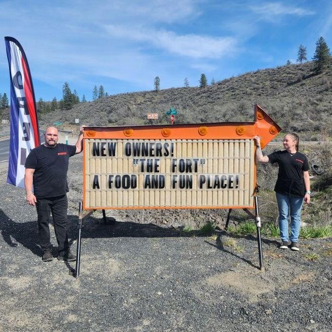 The Fort's owners standing beside a roadside sign announcing new owners